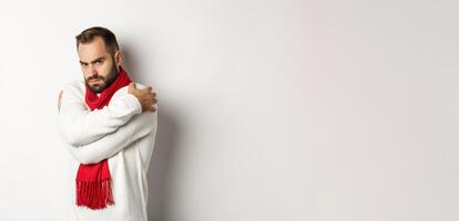 Offended guy embracing himself and looking displeased at camera, sulking while standing over white background photo