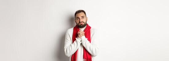 Christmas holidays and New Year concept. Sad and miserable man praying to God, making with and holding hands in pray, looking up at sky and begging, standing over white background photo