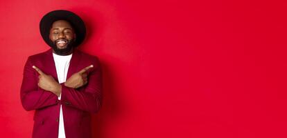 Happy young man dreaming and pointing fingers sideways, close eyes and smiling, showing two things, standing over red background photo