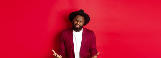 Frustrated and miserable african american man whining, complaining on life and crying, begging for something, standing over red background photo