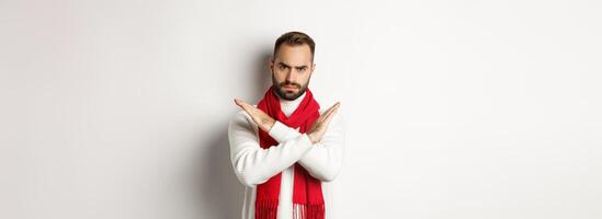 Angry bearded man frowning, showing cross stop gesture, telling no, forbid something bad, standing over white background photo