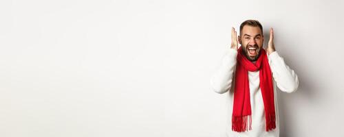 Christmas holidays and New Year concept. Angry man in scream and shout, shaking hands near head with frustrated expression, standing over white background photo