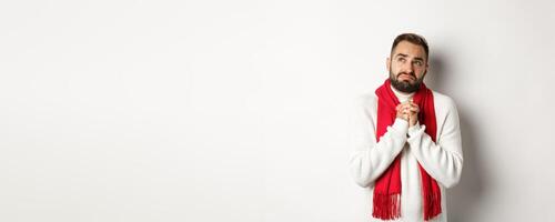 Christmas holidays and New Year concept. Sad and miserable man praying to God, making with and holding hands in pray, looking up at sky and begging, standing over white background photo