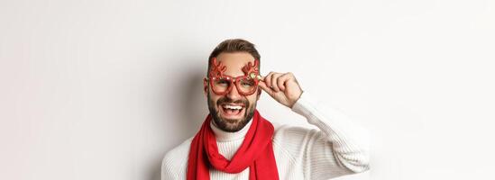 Christmas, New Year and celebration concept. Happy bearded guy in party glasses laughing and enjoying winter holidays, white background photo