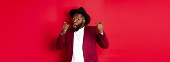 Christmas and people concept. Happy Black man celebrating New Year and dancing, wearing party outfit, red background photo