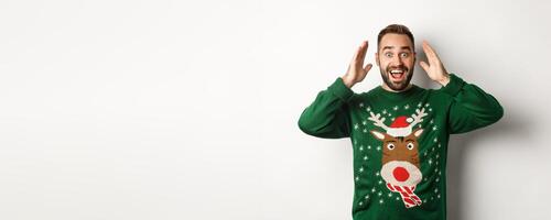 Christmas, holidays and celebration. Surprised man open eyes and see a gift, standing happy against white background photo