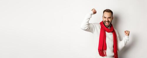 Christmas holidays and New Year concept. Happy bearded man celebrating and enjoying party, raising hands up in triumph, rejoicing while standing over white background photo