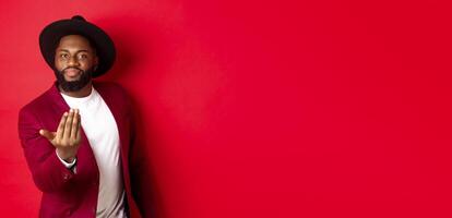 Handsome and masculine Black man asking come closer, luring to step forward, calling for you, standing over red background photo