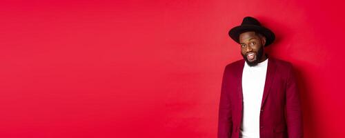 Christmas shopping and people concept. Handsome bearded african american guy looking at camera, smiling confident, wearing party clothes, red background photo