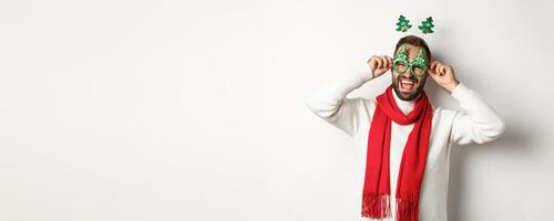 Christmas, New Year and celebration concept. Handsome guy celebrating, put on party glasses and accessory, laughing happy, standing over white background photo