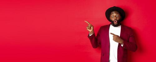 Winter holidays and shopping concept. Happy Black man pointing left and smiling, showing new year promo offer on red background photo