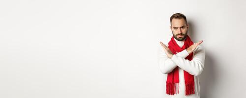 Angry bearded man frowning, showing cross stop gesture, telling no, forbid something bad, standing over white background photo