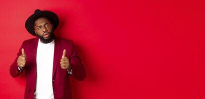 Impressed Black man saying good job, cheer up with thumbs-up, praise something, standing against red background photo