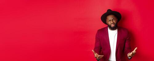 Frustrated and miserable african american man whining, complaining on life and crying, begging for something, standing over red background photo