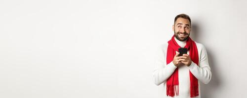 Man thinking while texting message on mobile phone, smiling and standing over white background photo