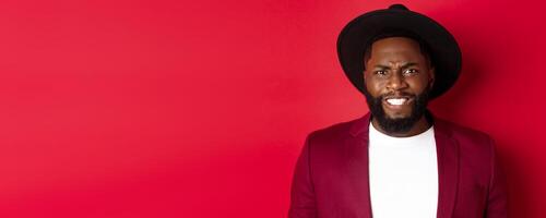 Close-up of Black man feeling uncomfortable, grimacing as watching something painful, cringe and frowning, standing over red background photo
