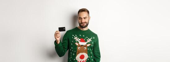 Christmas holidays and shopping concept. Thoughtful man looking at credit card, thinking and standing over white background photo