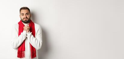 Christmas holidays and New Year concept. Sad man begging for help, holding hands in pray and looking distressed at camera, asking for favour, standing over white background photo