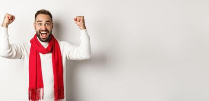 Christmas holidays and New Year concept. Excited man rejoicing, winning prize, raising hands up and looking relieved, triumphing, standing over white background photo