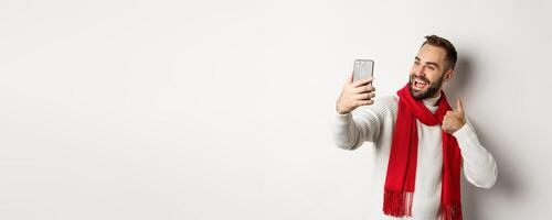 Happy bearded man call and showing thumbs up at mobile phone, like christmas gift, talking online, standing over white background photo