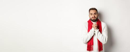 Christmas holidays and New Year concept. Sad man begging for help, holding hands in pray and looking distressed at camera, asking for favour, standing over white background photo