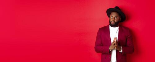 Serious looking man getting ready to business, holding hands pressed together and nervously staring at camera, listening closely, standing against red background photo