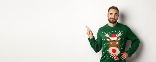 Winter holidays and christmas. Thoughtful bearded man thinking, having an idea and pointing finger at upper left corner, white background photo