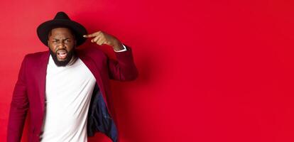 Angry Black man scolding person for being stupid, pointing at head and looking pissed-off, standing against red background photo