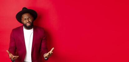 Frustrated and miserable african american man whining, complaining on life and crying, begging for something, standing over red background photo