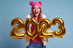 Beautiful woman in winter coat holding gold colored numbers and smiling against blue background photo
