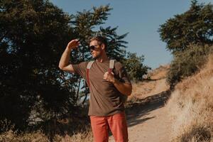 Confident adventurer with backpack covering face from sun while standing on the mountain footpath photo