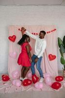 Romantic young African couple dancing on pink fabric background with heart shaped balloons photo