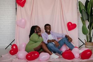 Beautiful young African couple bonding and smiling while sitting on decorated pink fabric background photo