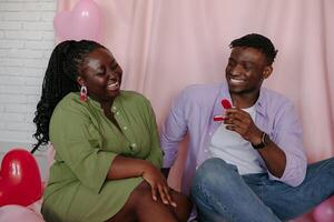 Handsome African man giving engagement ring while proposing his girlfriend to marry him on pink background photo