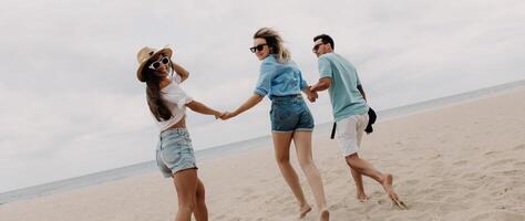 Three joyful friends spending fun time while running by the beach to the sea together photo
