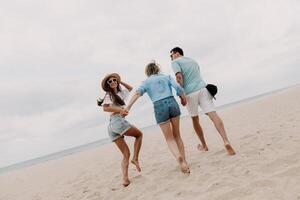 Three happy young friends spending fun time while running by the beach to the sea together photo
