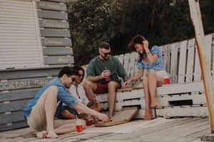 Group of happy friends enjoying food and drinks while relaxing near the beach cafe together photo
