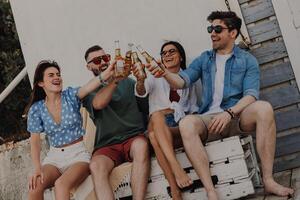 Group of joyful young friends toasting with beer while spending carefree time outdoors together photo