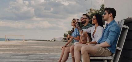 Group of joyful friends enjoying sea view while spending time near the beach house together photo