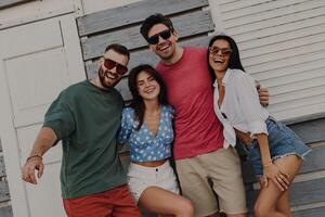 Group of joyful friends bonding and smiling while standing near the beach house outdoors photo