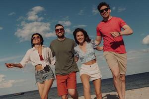 Group of happy friends bonding and smiling while running by the beach together photo