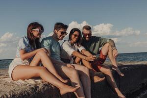 Group of young people looking at smart phone and smiling while enjoying time seaside together photo