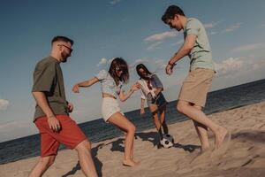 Group of happy young people spending fun time while playing soccer on the beach together photo