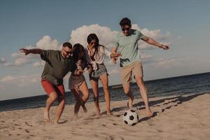 Group of young people playing soccer and having fun on the beach together photo