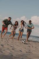 Group of happy young people spending carefree time together while playing beach soccer photo