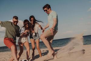 Group of cheerful young friends playing soccer and having fun on the beach together photo