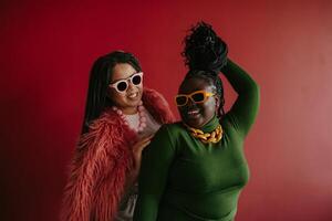 Two joyful plus size African woman playing with their braided hair while having fun on red background photo