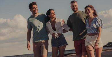 Group of cheerful young friends bonding and smiling while walking by the beach together photo