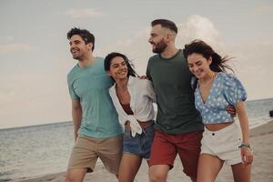 Group of beautiful young people bonding and smiling while walking by the beach together photo