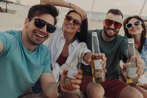 Group of happy young people making selfie while enjoying beer on the beach together photo